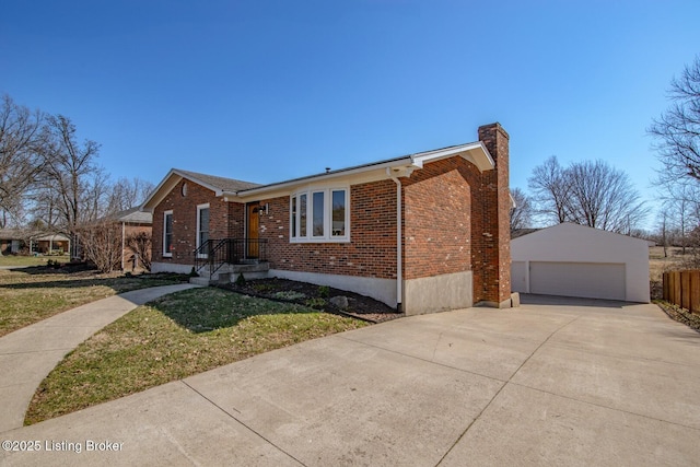 view of front of home featuring brick siding, a detached garage, a front yard, a chimney, and an outbuilding