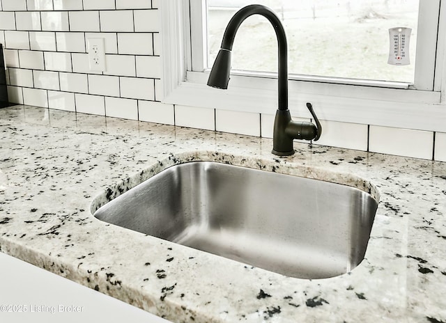 details with a sink, light stone countertops, and backsplash