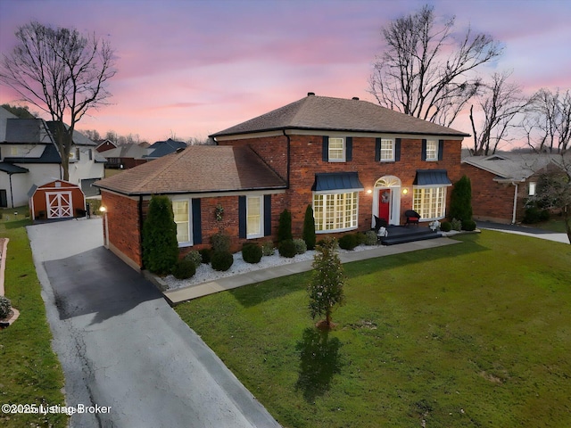 view of front of house featuring driveway, a yard, an outdoor structure, a shingled roof, and brick siding