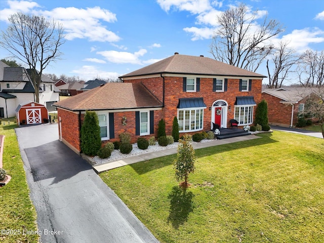 view of front of home with a front yard, an outbuilding, roof with shingles, aphalt driveway, and brick siding