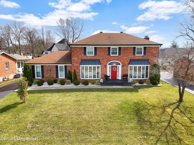 view of front of home with a front lawn, brick siding, roof with shingles, and a chimney