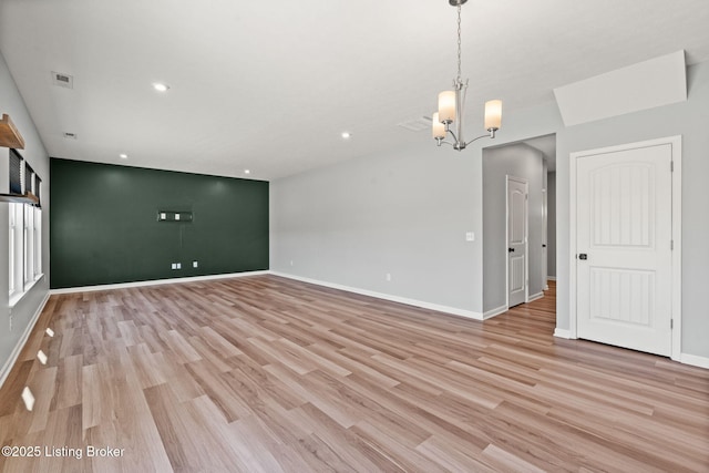 empty room featuring a notable chandelier, light wood-style floors, visible vents, and baseboards