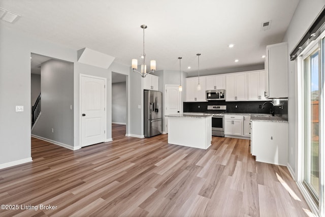 kitchen with a center island, light wood-type flooring, decorative backsplash, white cabinets, and stainless steel appliances