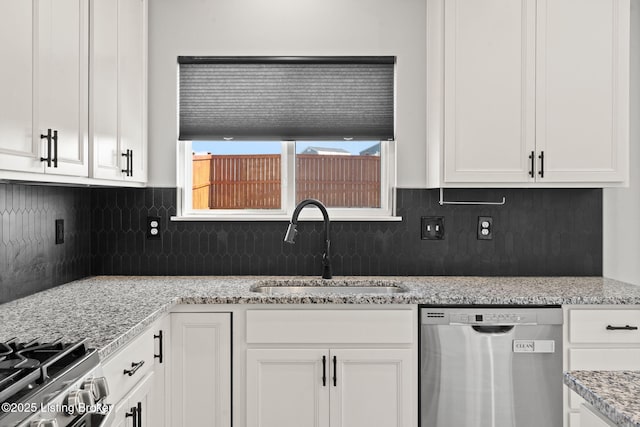 kitchen featuring light stone counters, a sink, white cabinets, stainless steel dishwasher, and tasteful backsplash