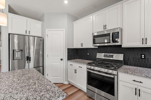 kitchen with light stone counters, decorative backsplash, appliances with stainless steel finishes, white cabinetry, and light wood-type flooring