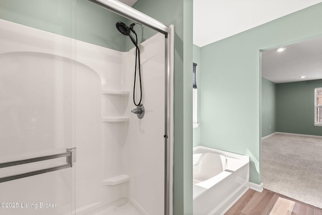 full bathroom featuring a bath, a shower stall, baseboards, and wood finished floors