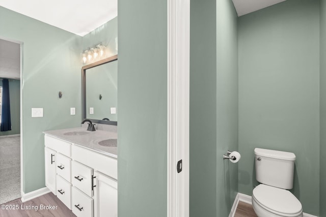 bathroom with a sink, toilet, wood finished floors, and double vanity