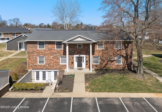 view of front of property with brick siding, a front lawn, and uncovered parking