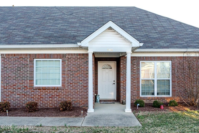 entrance to property featuring brick siding and a shingled roof