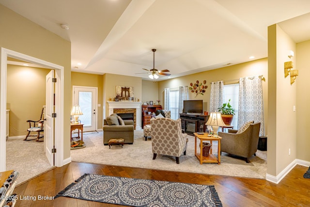 living area featuring a glass covered fireplace, a raised ceiling, baseboards, and wood-type flooring