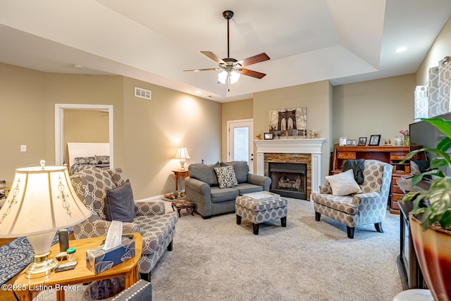 living area with visible vents, carpet floors, a fireplace, a raised ceiling, and a ceiling fan