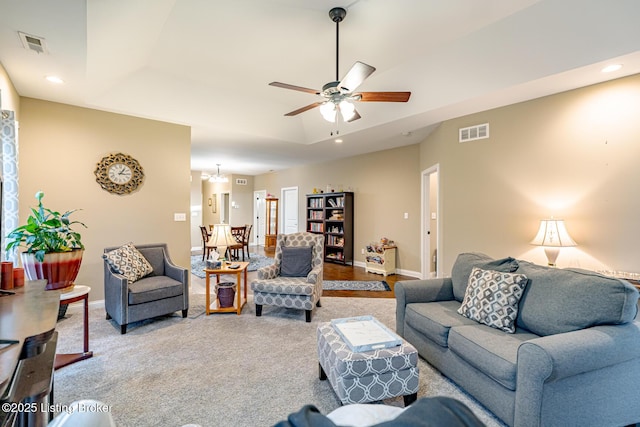 living room with a tray ceiling, recessed lighting, visible vents, and baseboards