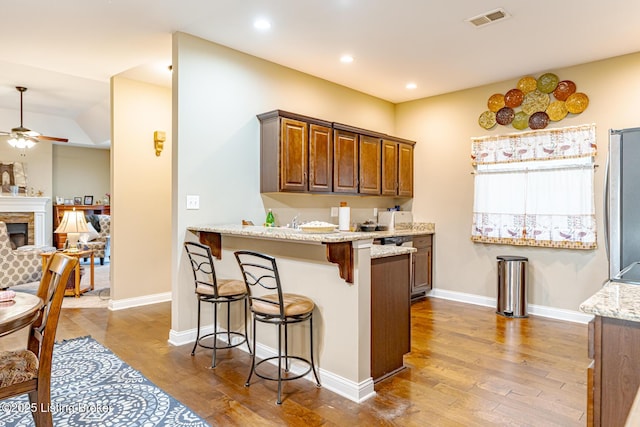 kitchen featuring light stone countertops, a fireplace, a breakfast bar, and wood finished floors