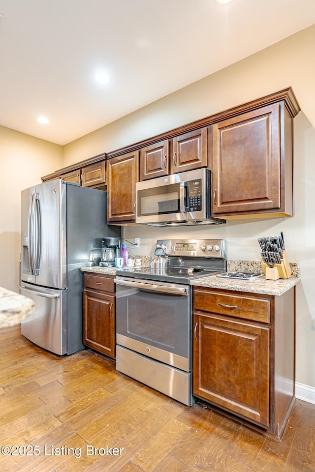 kitchen with light wood-type flooring, recessed lighting, appliances with stainless steel finishes, baseboards, and light stone countertops