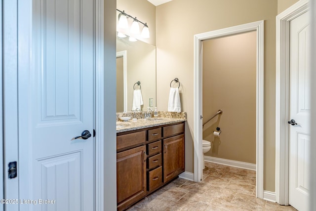 bathroom featuring a sink, baseboards, toilet, and double vanity