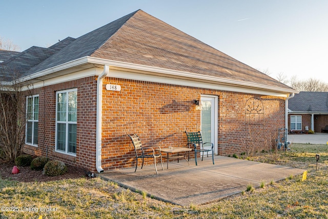 back of house featuring brick siding, a patio, and roof with shingles