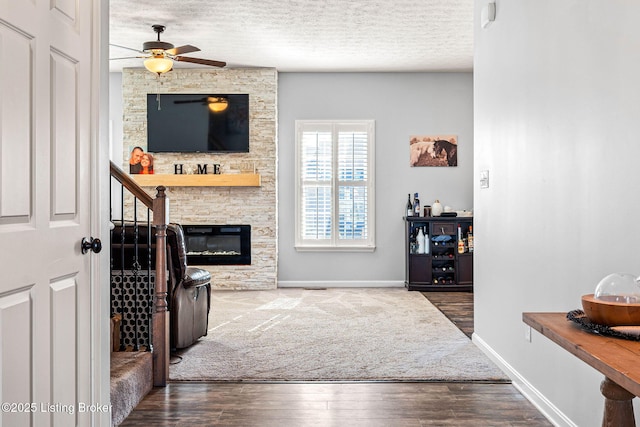 living room featuring ceiling fan, baseboards, a fireplace, wood finished floors, and a textured ceiling