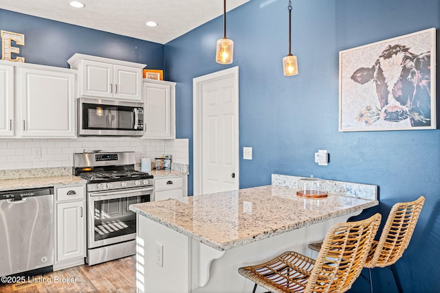 kitchen with backsplash, light wood-type flooring, a kitchen bar, appliances with stainless steel finishes, and white cabinetry