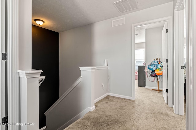 hall featuring an upstairs landing, visible vents, a textured ceiling, and carpet floors