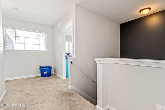 corridor featuring visible vents, baseboards, a textured ceiling, carpet flooring, and an upstairs landing