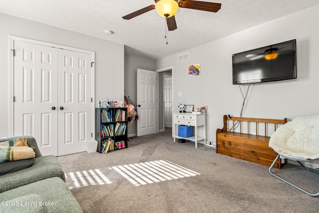 carpeted living area with a ceiling fan, visible vents, and a textured ceiling