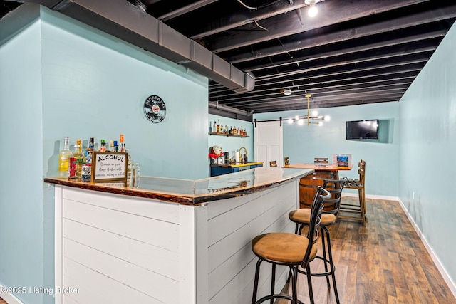 bar featuring dark wood finished floors, a dry bar, a barn door, and baseboards