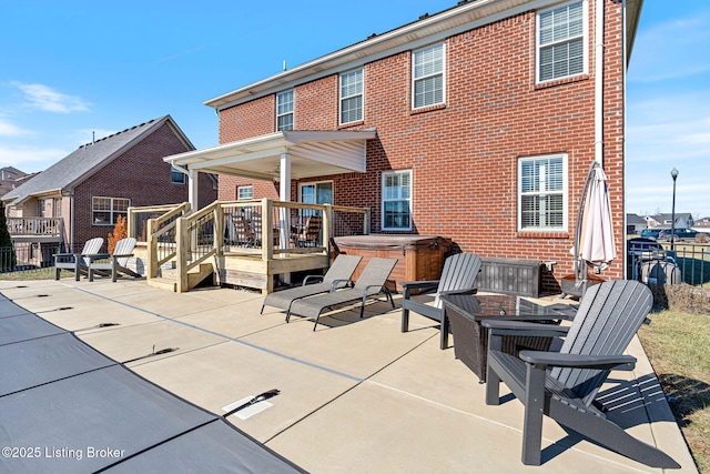 rear view of house featuring brick siding, a patio area, a hot tub, and fence