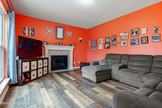 living area featuring a fireplace, a textured ceiling, baseboards, and wood finished floors