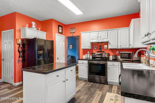 kitchen with dark countertops, stainless steel appliances, under cabinet range hood, and a sink