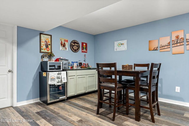 dining area with wine cooler, baseboards, a bar, and dark wood finished floors