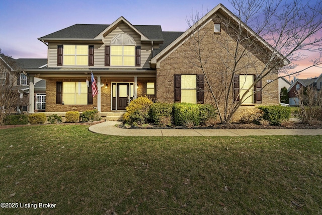 view of front of house with a porch, a lawn, and brick siding