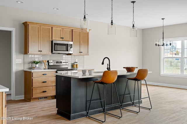 kitchen featuring a kitchen island with sink, stainless steel appliances, light wood-style floors, light countertops, and decorative backsplash