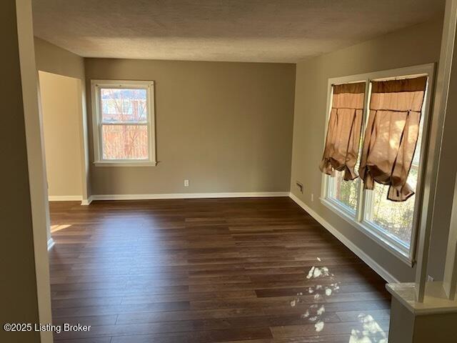 empty room with dark wood-style floors, a textured ceiling, and baseboards