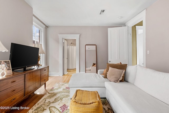 bedroom featuring visible vents, ensuite bath, baseboards, and wood finished floors