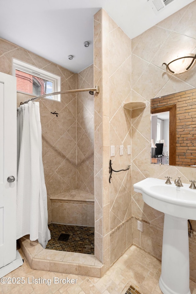 bathroom with visible vents, tiled shower, and tile walls