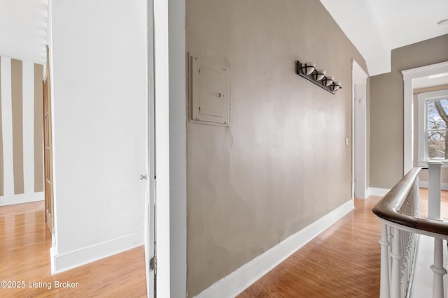 hallway featuring electric panel, light wood-type flooring, and baseboards