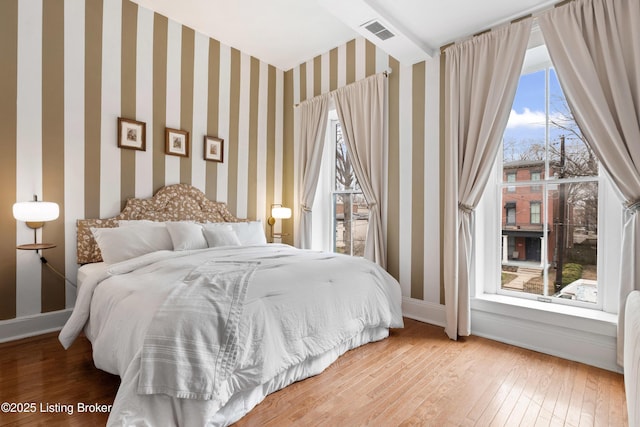 bedroom with visible vents, wallpapered walls, baseboards, and hardwood / wood-style flooring