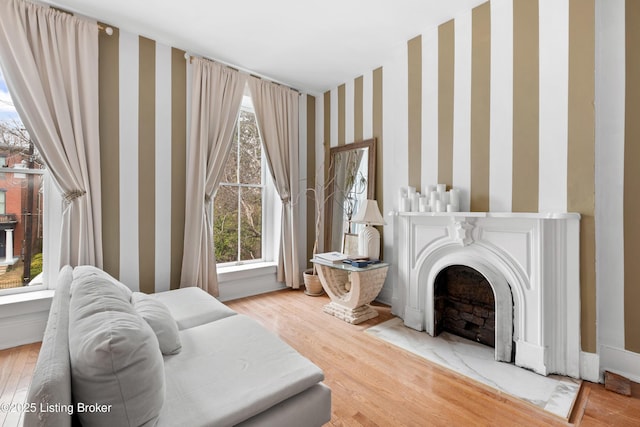 living area featuring a fireplace with flush hearth, wallpapered walls, baseboards, and wood finished floors