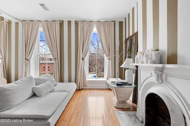 living area featuring a wealth of natural light, visible vents, light wood-style flooring, and wallpapered walls