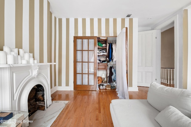 living area featuring visible vents, wallpapered walls, baseboards, and wood finished floors