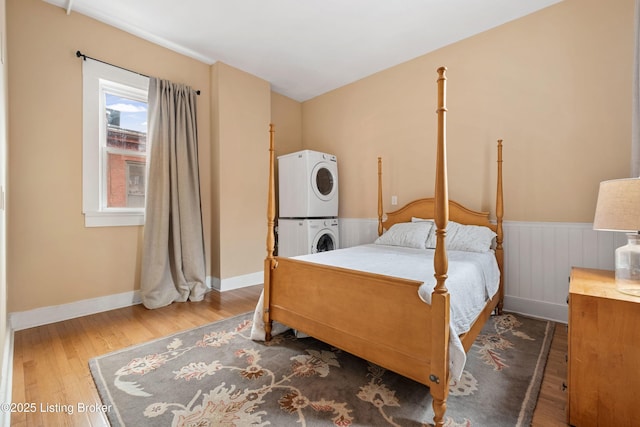 bedroom featuring stacked washer / dryer, a wainscoted wall, baseboards, and wood finished floors