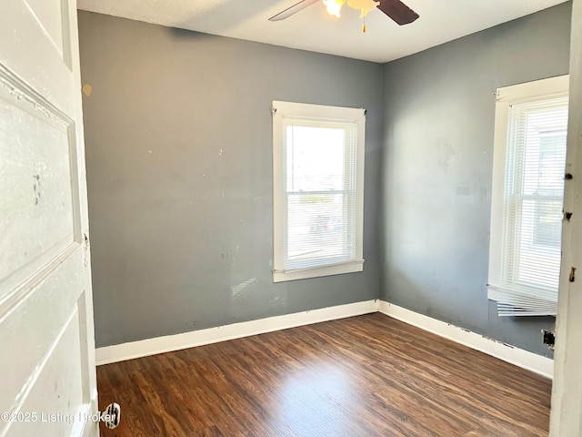 empty room featuring dark wood finished floors, a ceiling fan, and baseboards