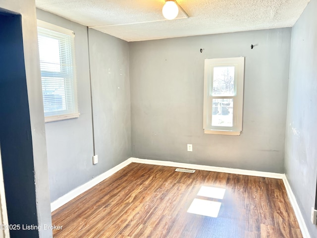 empty room featuring visible vents, baseboards, a textured ceiling, and wood finished floors