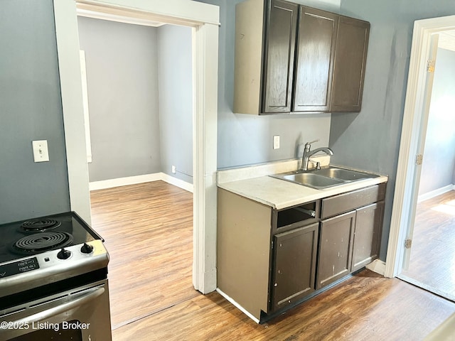 kitchen featuring baseboards, stainless steel electric range, a sink, light countertops, and light wood-type flooring