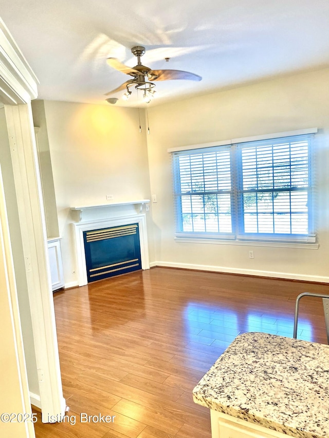 unfurnished living room with a glass covered fireplace, wood finished floors, baseboards, and ceiling fan