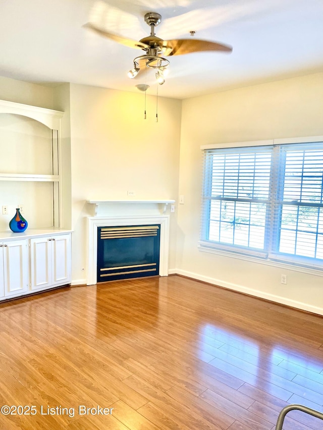 unfurnished living room featuring baseboards, wood finished floors, a glass covered fireplace, and a ceiling fan