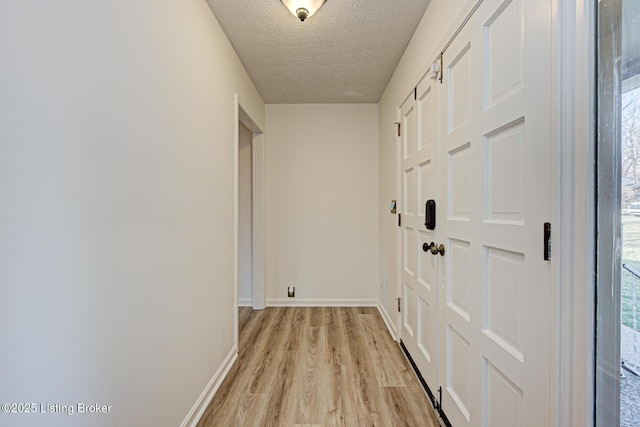 hallway with light wood-type flooring, baseboards, and a textured ceiling