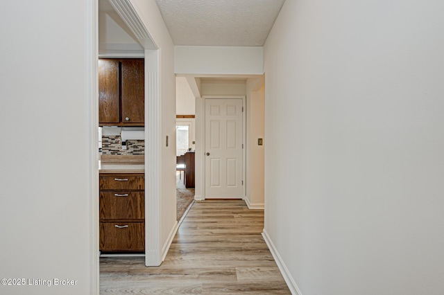 hall with baseboards, light wood-type flooring, and a textured ceiling