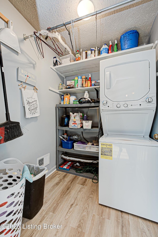 laundry room featuring stacked washer / drying machine, visible vents, wood finished floors, and laundry area