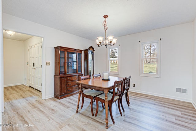 dining space featuring a notable chandelier, baseboards, visible vents, and light wood-type flooring